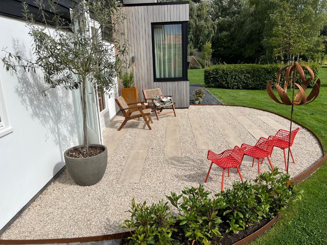 Verzorgde tuin met grindterras, border en zitje bij een olijfboom