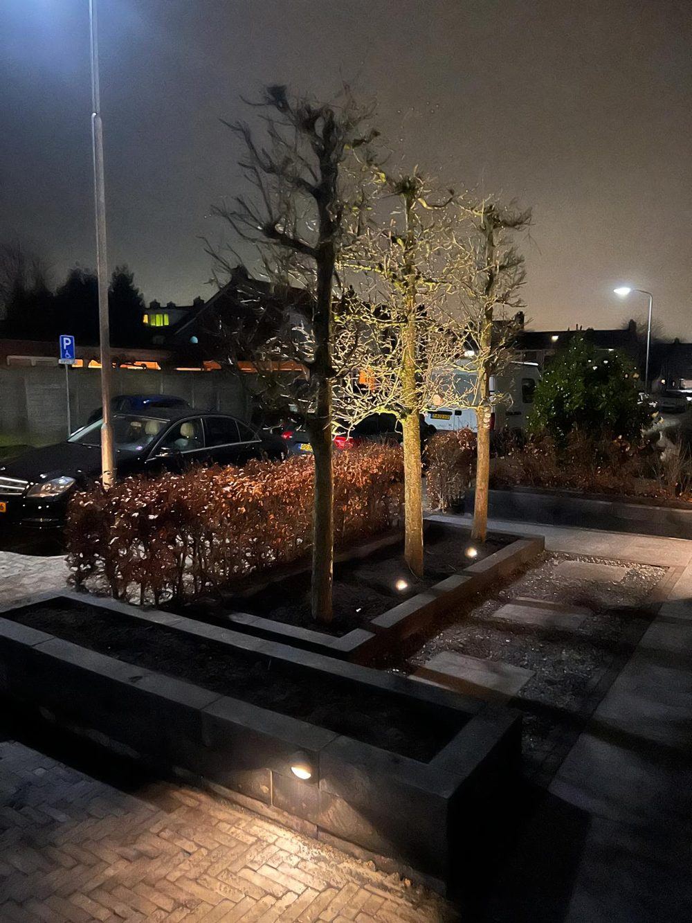 Tuin in avondsfeer met een corten stalen sierobject en sfeervolle verlichting