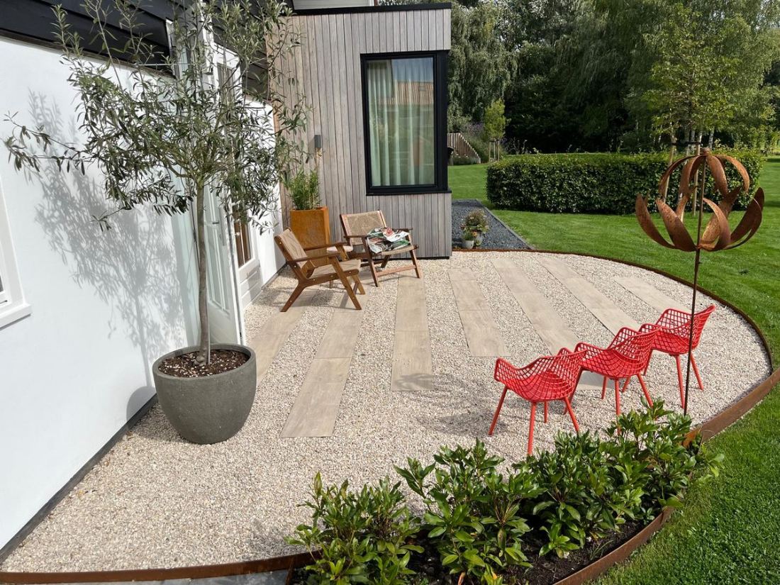 Rond grindterras met olijfboom, rode designstoelen en corten-stalen rand