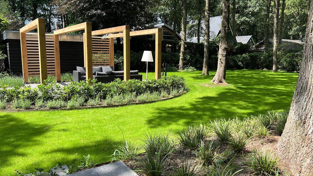 Loungehoek met houten pergola en zithoek in een bosrijke tuin met gazon